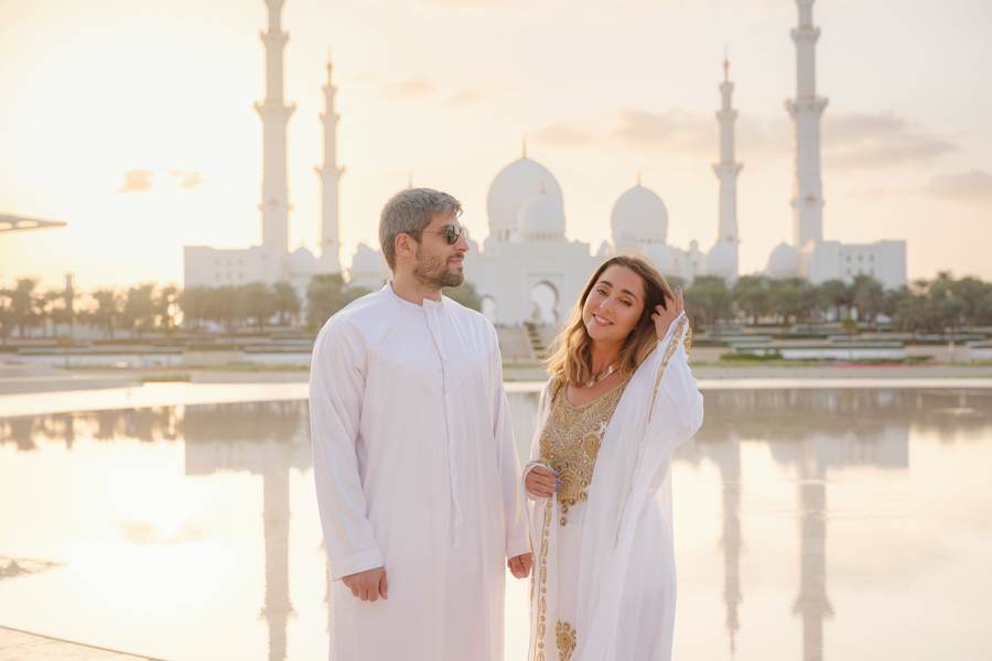 Couple in traditional dress in front of Sheikh Zayed Grand Mosque at sunset