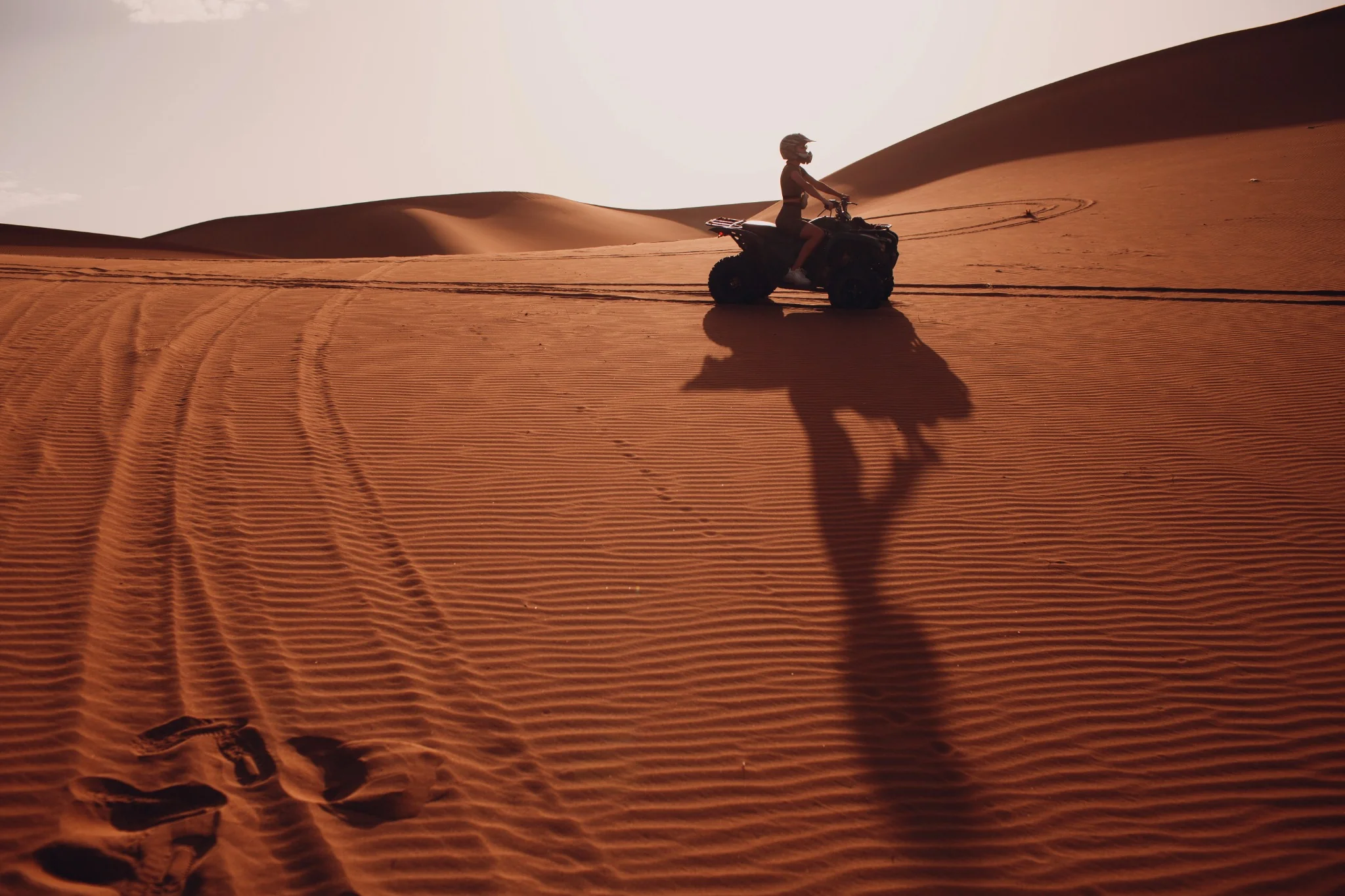 Quad bike rider casting a long shadow across desert dunes
