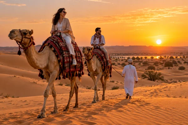 Visitors riding camels across Abu Dhabi desert dunes at sunset