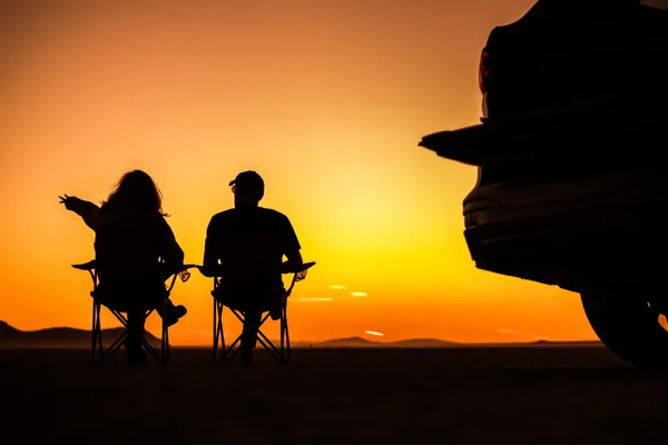 Couple watching sunset beside a 4x4 during an overnight Liwa desert camping trip