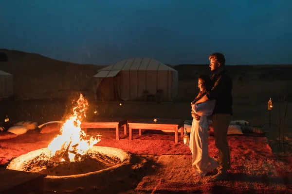 Couple standing beside a campfire at a private Liwa desert camp in the Empty Quarter