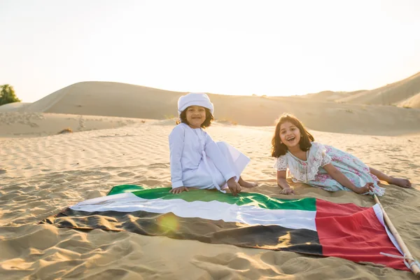 Children relaxing beside the UAE flag on the sand during a family Liwa desert tour from Abu Dhabi