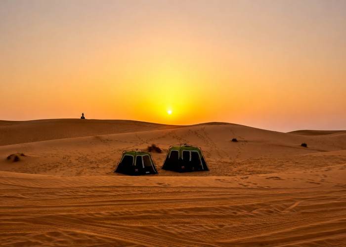 Two desert camping tents pitched among the dunes at sunset